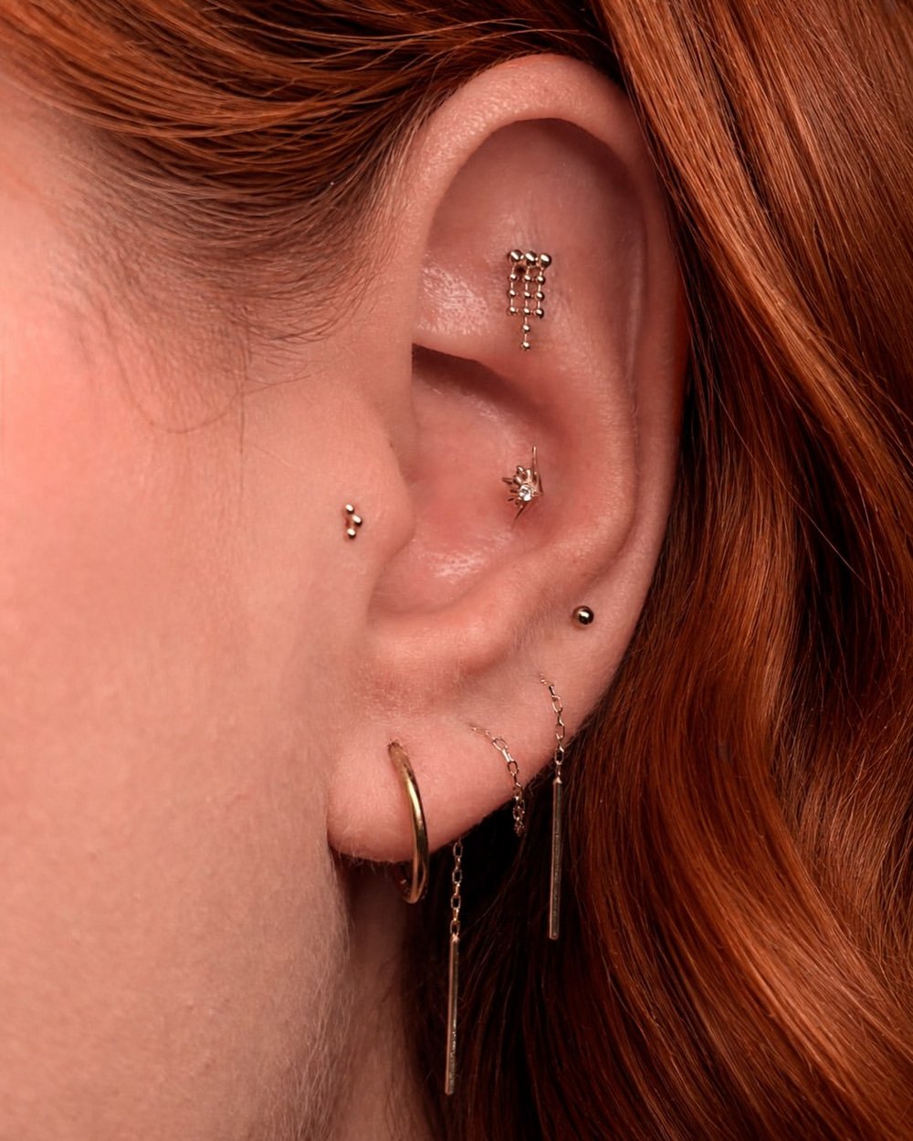 Ear with several piercings and gold jewelry in Barcelona - Circa Piercing